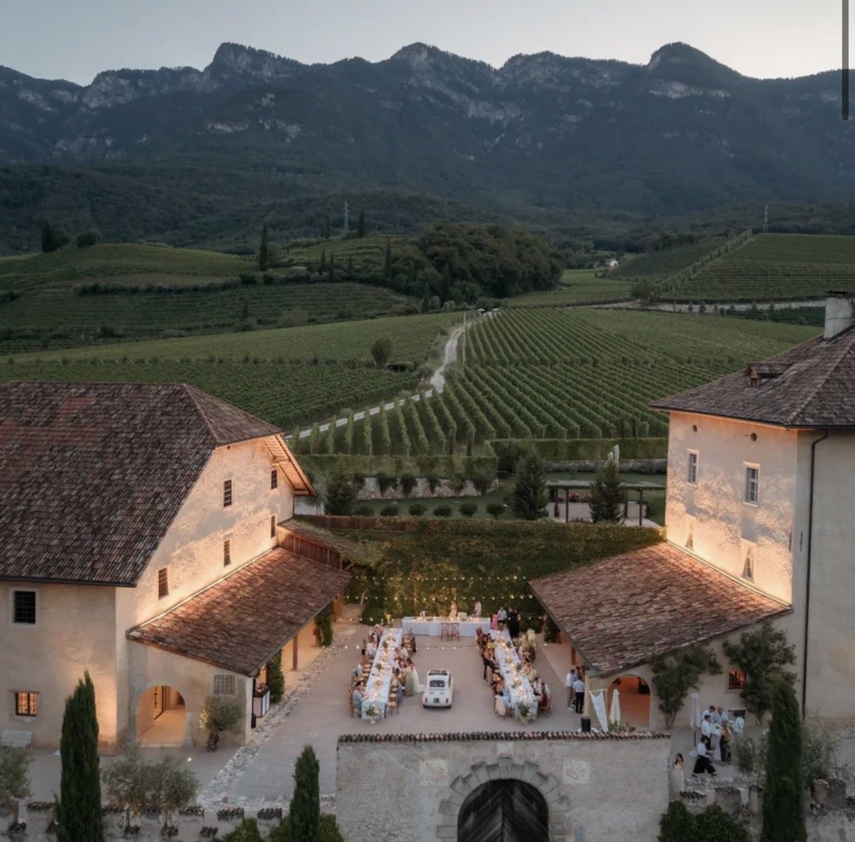 Der Innenhof von Gut Kaltenburg am Abend mit gedeckten Tafeln und Lichterketten, dahinter Weinberge und Berge